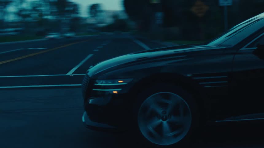 A black sedan travels along a dark road during dusk or dawn