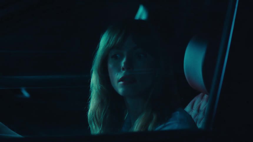 A woman is sitting inside of a parked car during the night time