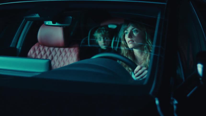 A woman and her child are stopped in their car as the boy sleeps