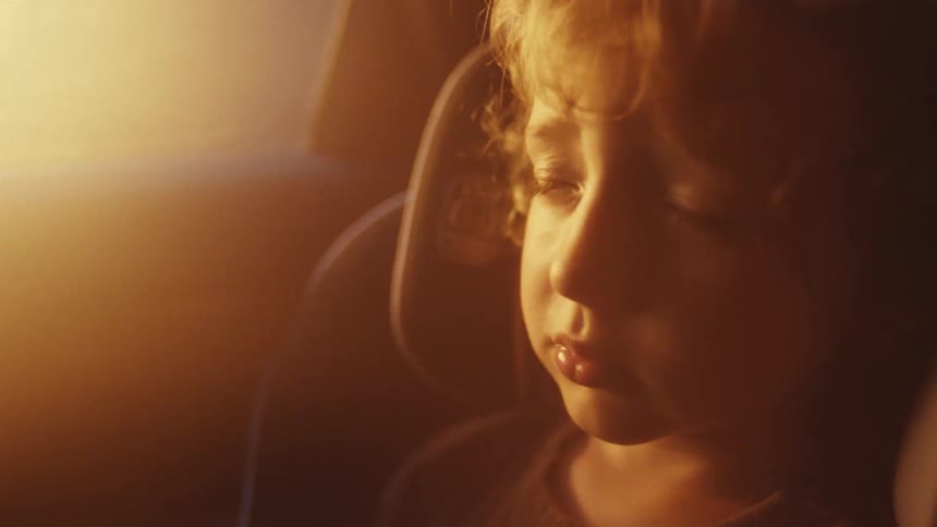 A little boy is sleeping in a car seat in a car as the sun is rising