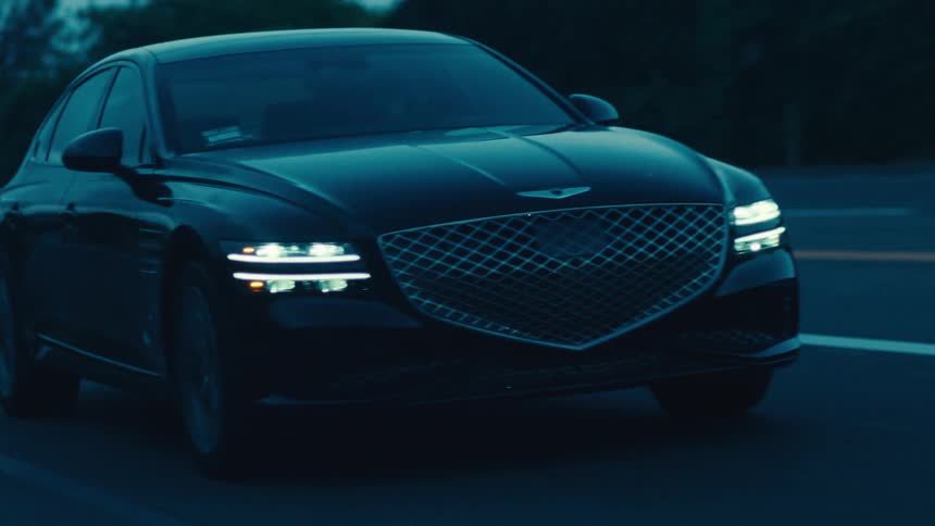 Dark sedan drives along a highway passing through a residential neighborhood after dusk