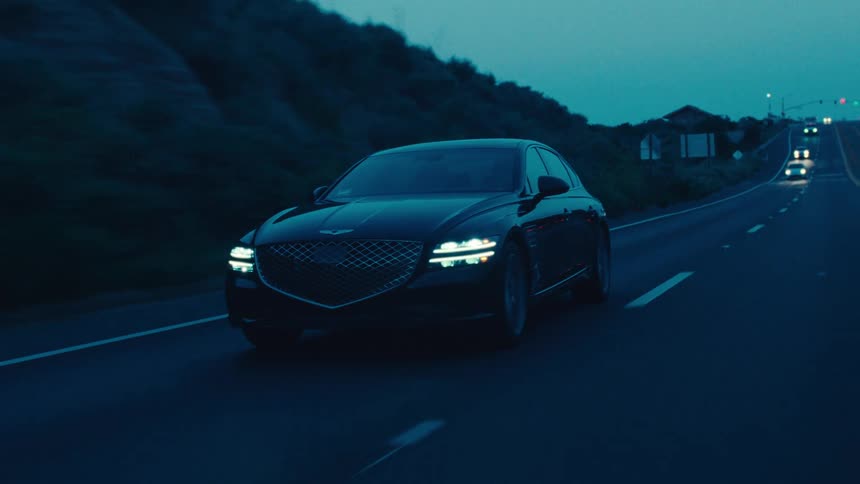 A black sedan travels along a dark road during dusk or dawn