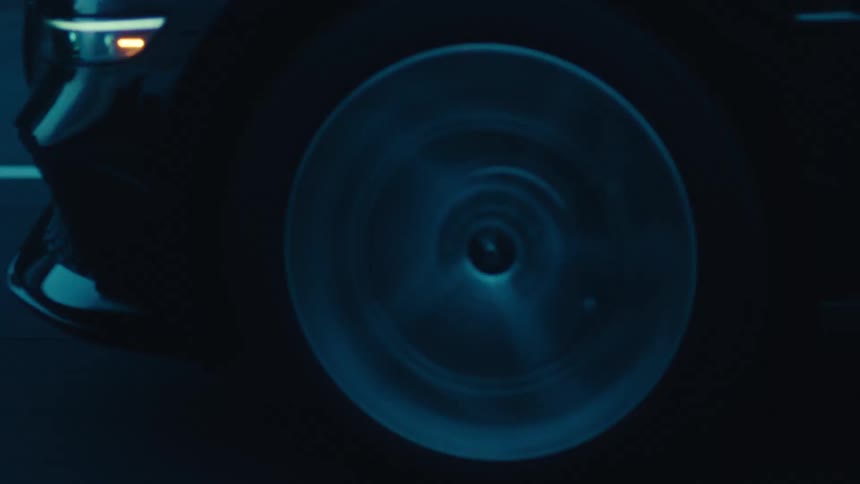 A close up of a sleek dark car speeding by with its headlights and wheel visible