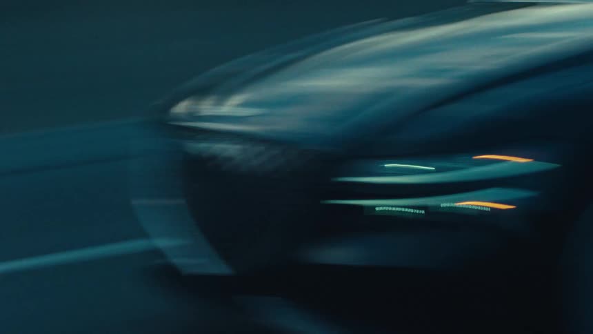 The front of a black sedan travels along a dark road during dusk or dawn