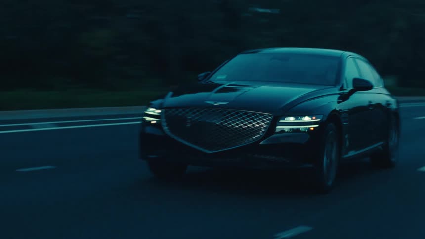 A black sedan travels along a dark road during dusk or dawn