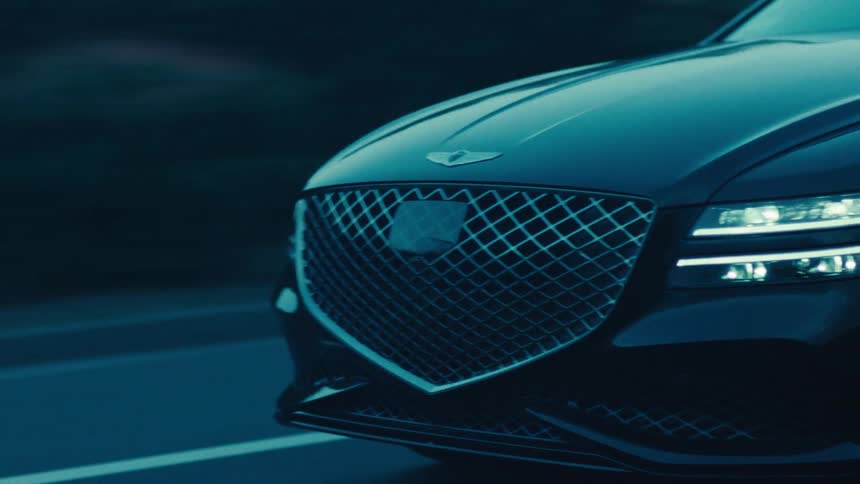 A black sedan travels along a dark road during dusk or dawn