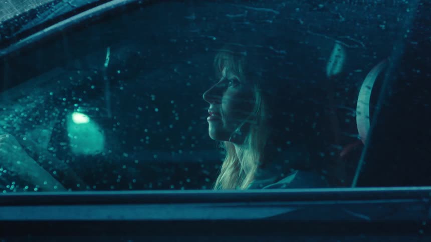 Side portrait of a blonde woman inside a vehicle at night with rain