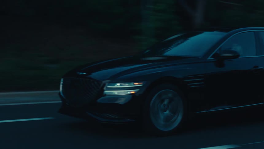 A black sedan travels along a dark road during dusk or dawn