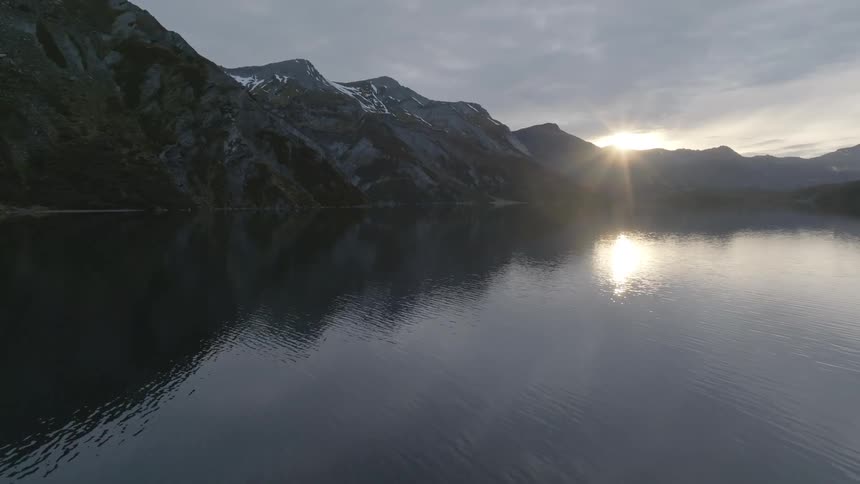 Sun reflecting off the lake as it sets behind the mountains at dusk