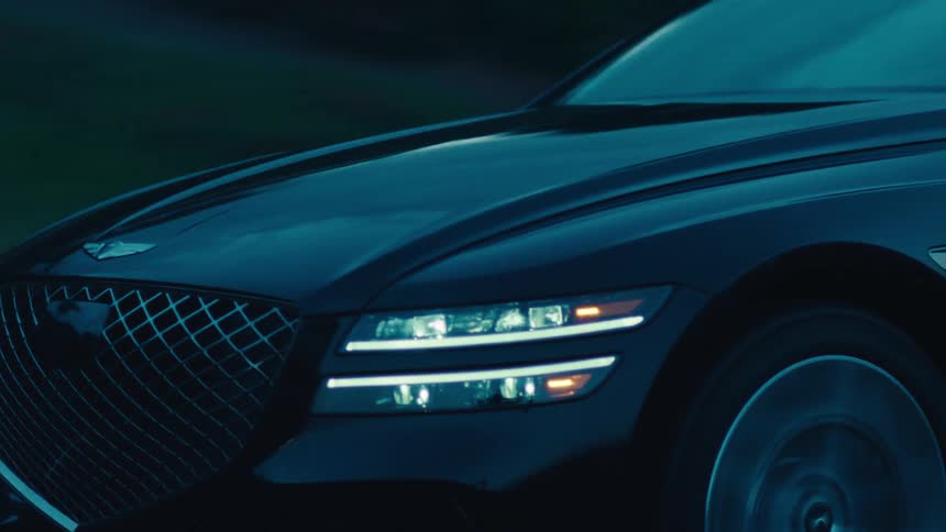 A black sedan travels along a dark road during dusk or dawn