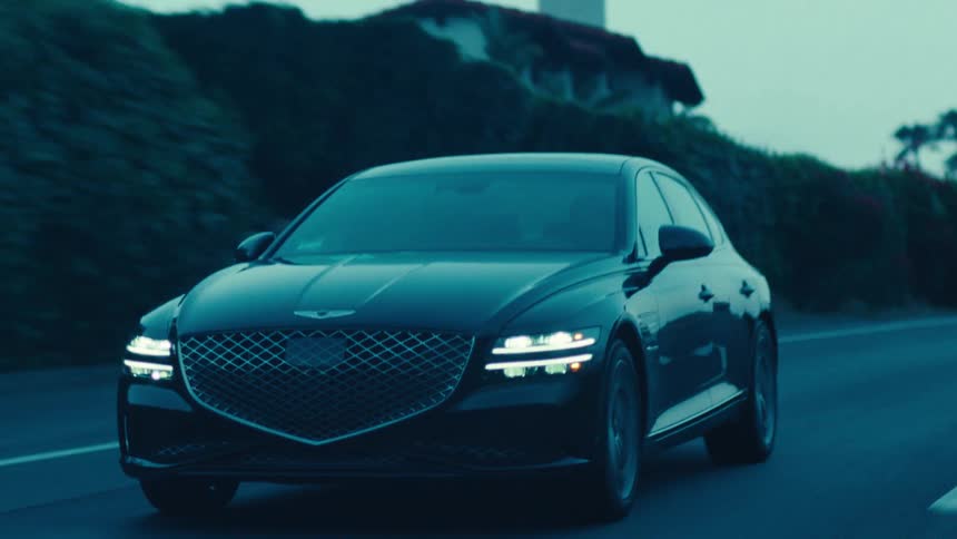 A black sedan drives along a rural highway at dusk
