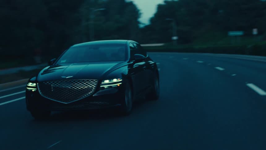 A black genesis suv drives down a dimly lit highway at dusk