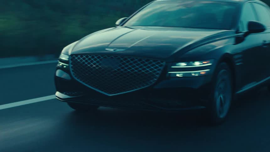 An adult drives a black sedan along a highway at sunrise