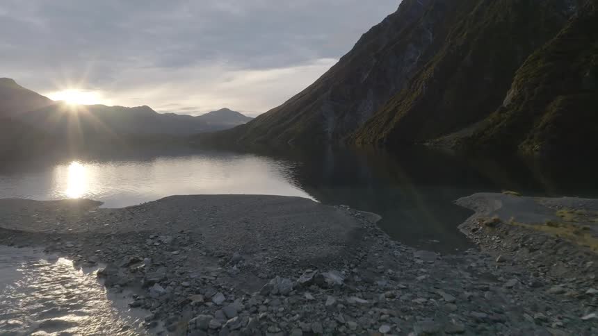 Aerial of creek gently flowing into lake as sun sets behind the mountains