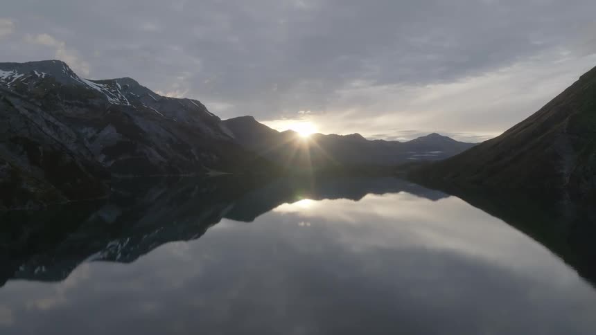 The sun is peeking over a mountain as it rises in a lake area
