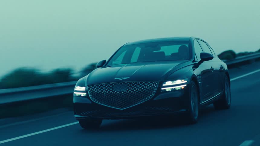 A black sedan moves along a coastal road during dusk or dawn