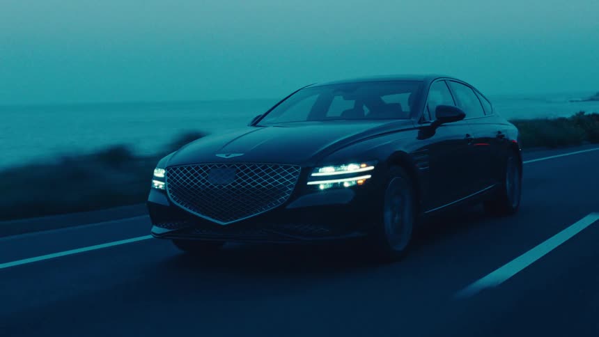 A dark sedan is driving very fast on a highway on the coast