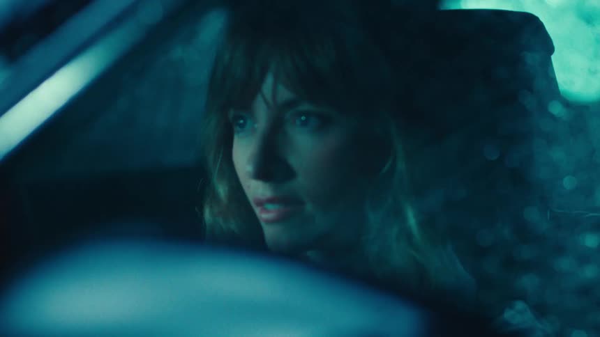 A woman sits inside her car while it rains and storms at night