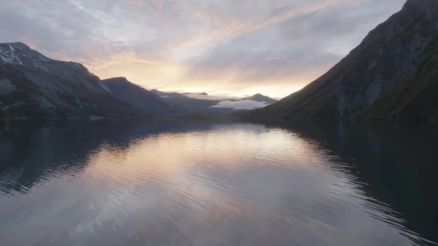 Flying slowly forward over a calm mountain lake reflecting the beautiful sunrisesunset sky between steep mountain slopes