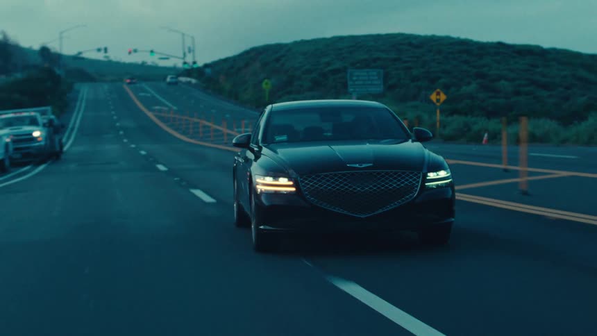 A black sedan travels along a dark road during dusk or dawn