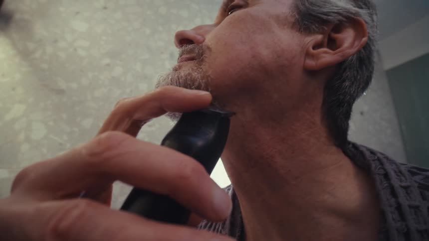 A man uses an electric razor to shave under their chin with the hand and neck area in focus