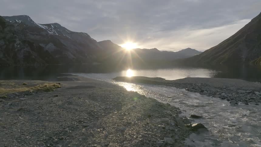 Creek flowing into lake as sun reflects off water at sunset