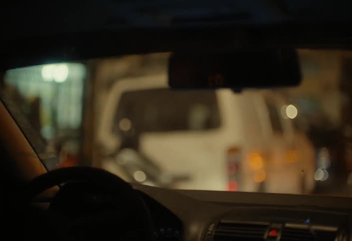 Man driving along a city street at night pulls up to the end of a line of cars