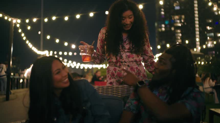 Three friends at an outdoor bar talking smiling and having glasses of drinks