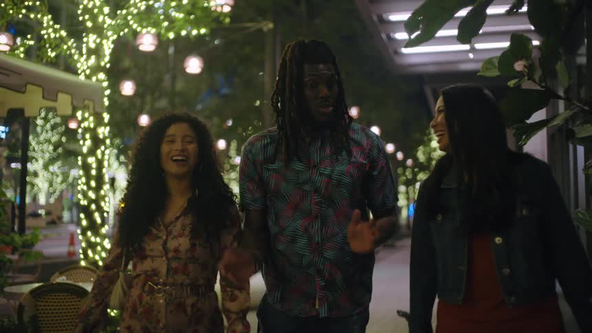 Three friends walking down a city sidewalk at night happily