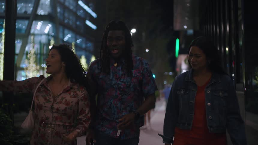 Three friends including a man and two women walk along the city sidewalks at night