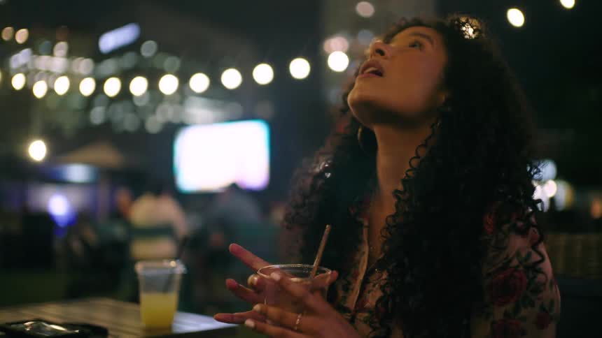 Curly haired woman sitting on a boat outdoors with a glass of drink at night