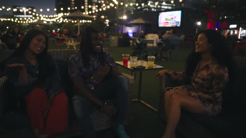 Three friends sitting chatting and having fun at an outdoor bar at night