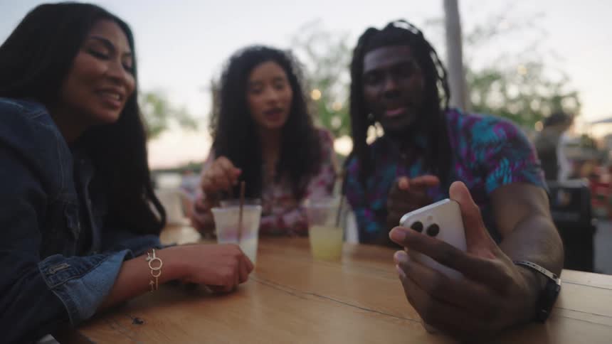 Friends sitting at a table with glasses of drink and interacting with a smartphone