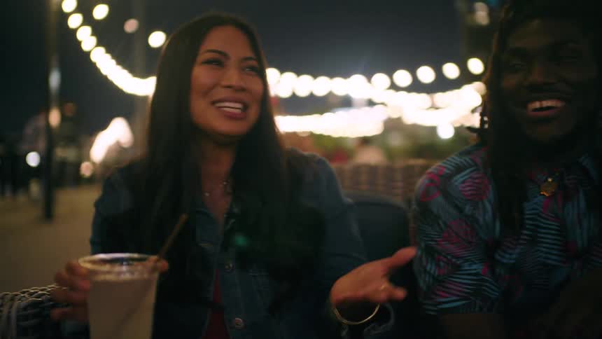 Two women with glasses of drink talking together with a man in a bar