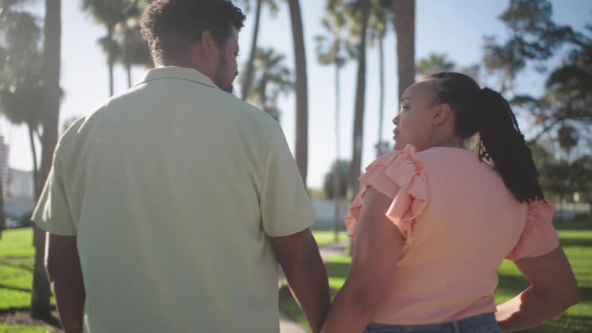 A couple holds hands while walking in a park in a tropical urban area