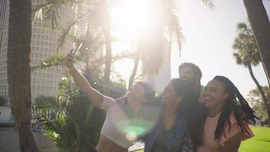 Group of four friends in a park with trees taking pictures