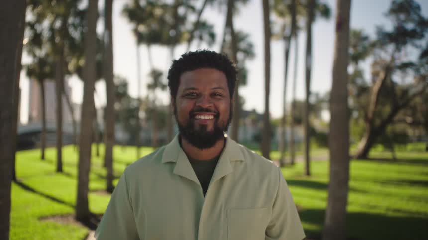 Man smiles while standing in an urban park on a summer day
