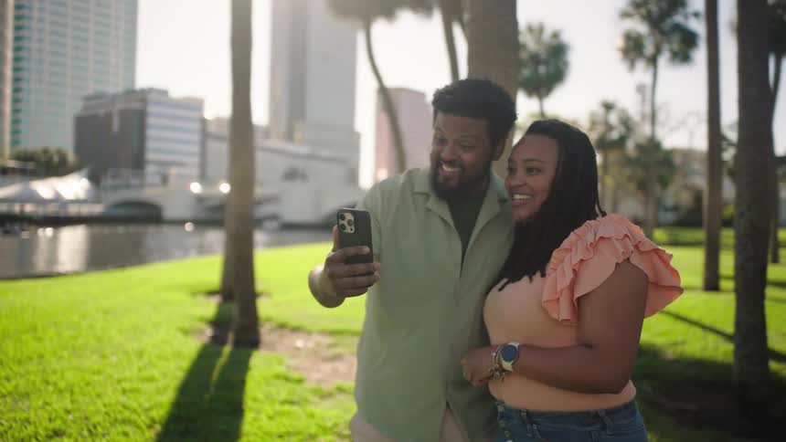Couple hugging taking a selfie in a park with palm trees