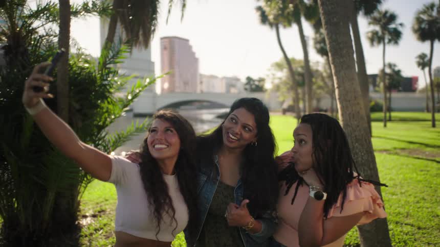 Friends take a group selfie while in a riverside park on a summer day