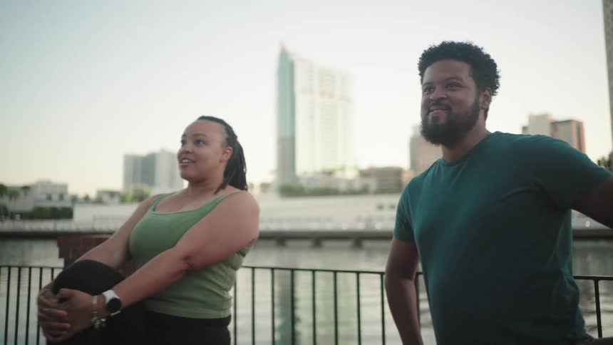 Woman stretches while she and a male friend stand near the river across from downtown
