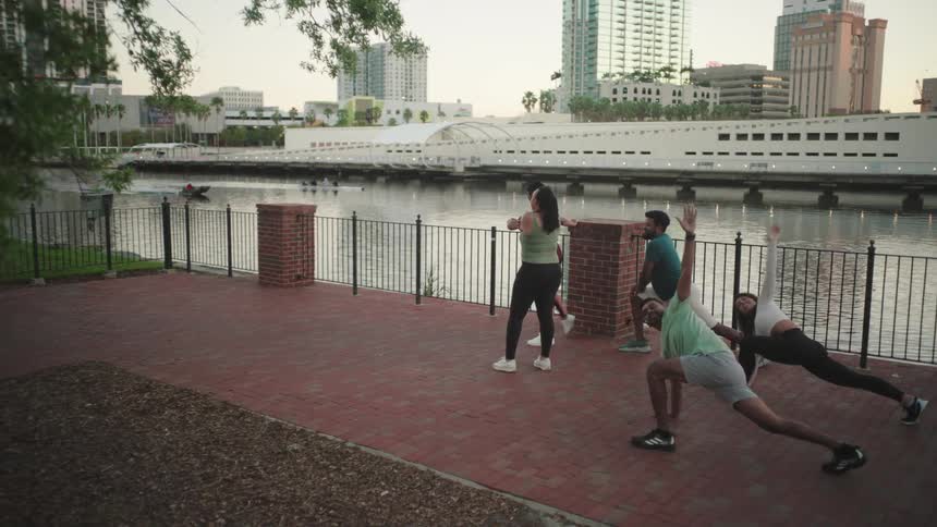 Group of five people on the shore of a lake in the city stretching their bodies