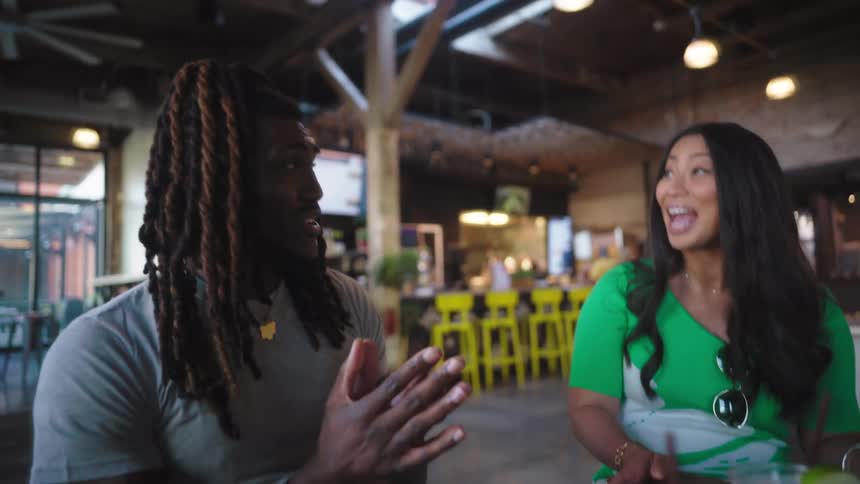 A group of people sit around talking and laughing with drinks in front of them at a bar