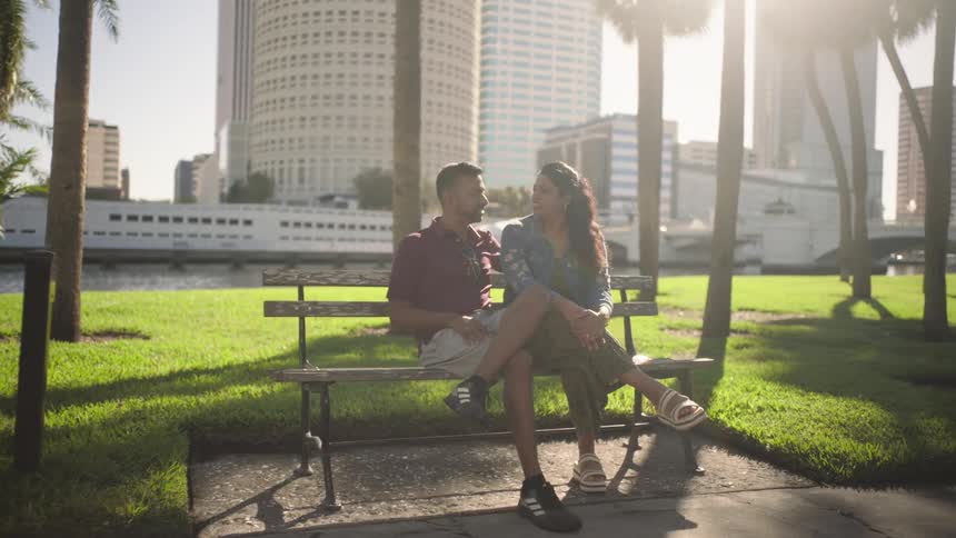 Couple sitting on bench at a waterfront park in the city having a conversation