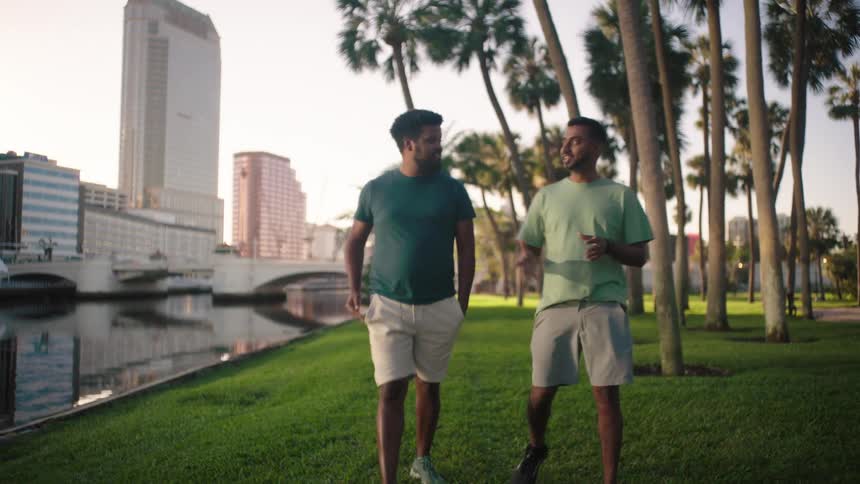 Two male friends walking at a waterfront park having a conversation in the summer