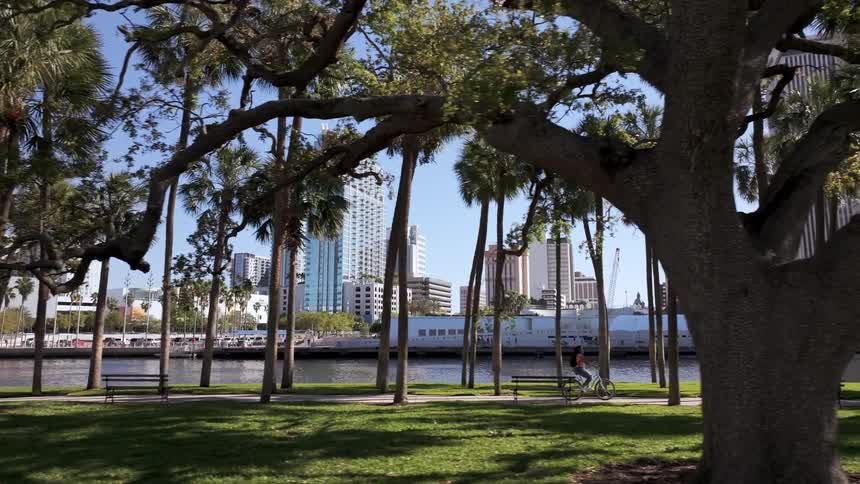 A teenage girl rides her bike down a sidewalk between city buildings and palm trees