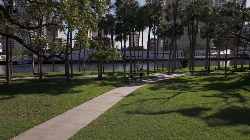 A girl rollerblades down a sidewalk in a park near city buildings