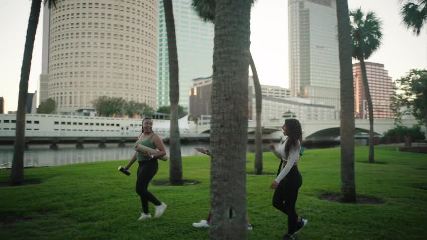 Three girlfriends dressed for yoga and carrying yoga mats walk through the city among buildings