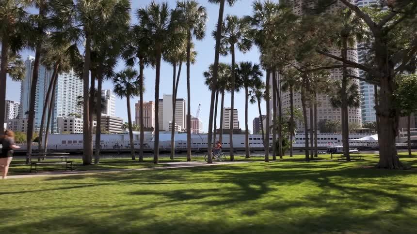 Person riding a bicycle through a wooded park with city buildings in the background