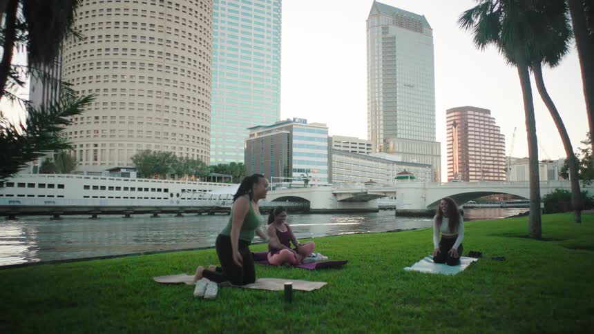Group of women relaxing on yoga mats after a workout on lawn near river in the city