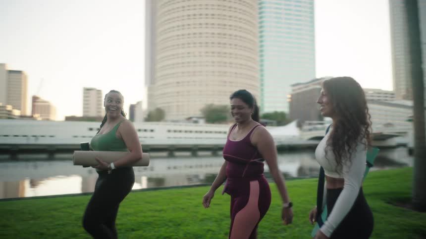 Three women walking outdoors in yoga clothes and equipment